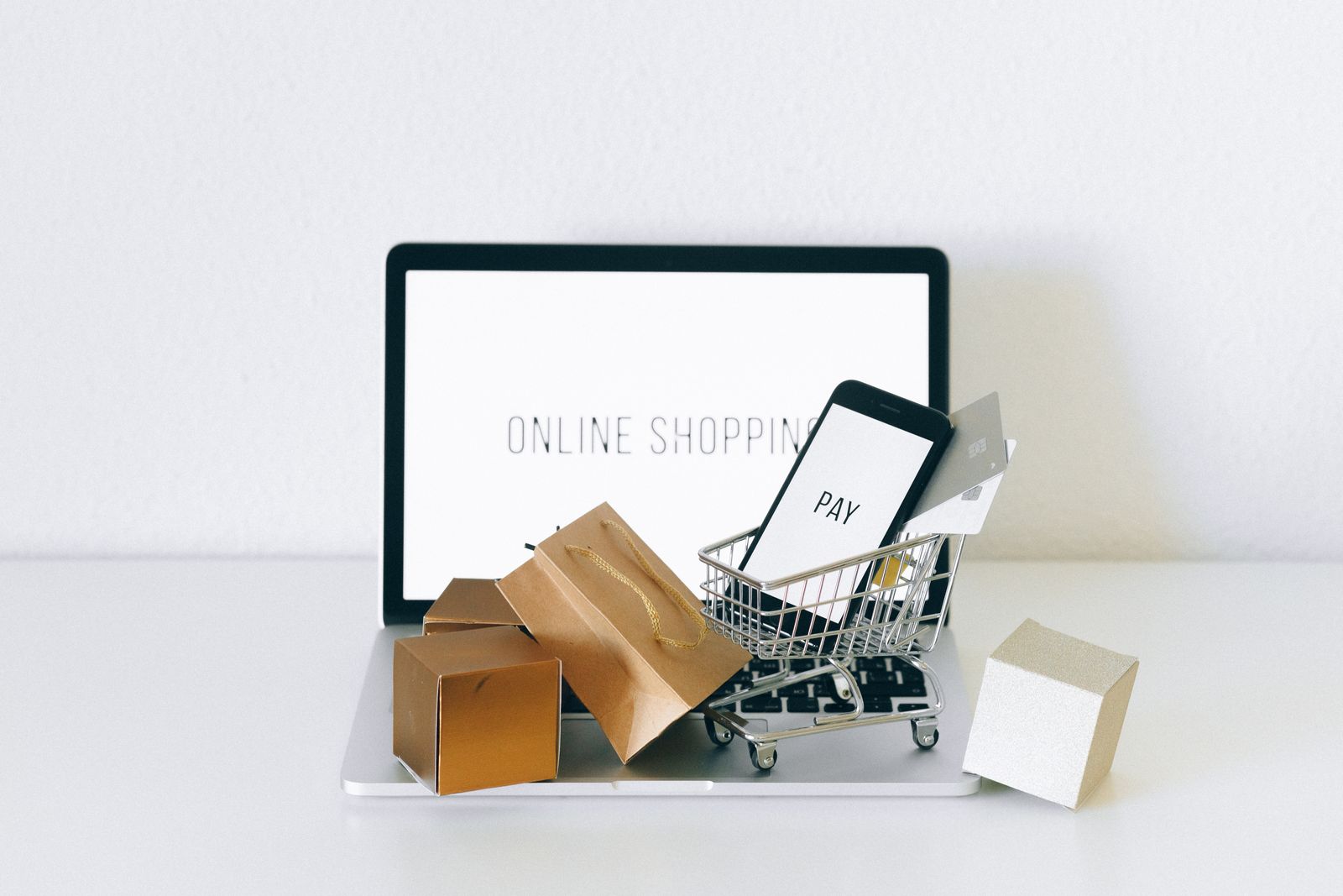 Online checkout on a laptop with a phone showing a pay screen in a miniature shopping cart.
